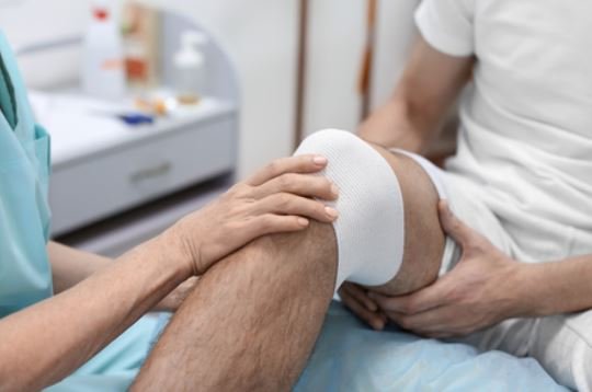 Doctor applies bandage to patient with knee injury